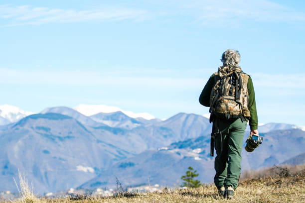 wanderer senior mann mit rucksack und kamera zu fuß auf dem bergweg - aktive reisende rentner mit grauen haaren - discovery reiseziel konzept, motivation - rückansicht mit kopierraum - behind photographer men mountain climbing stock-fotos und bilder