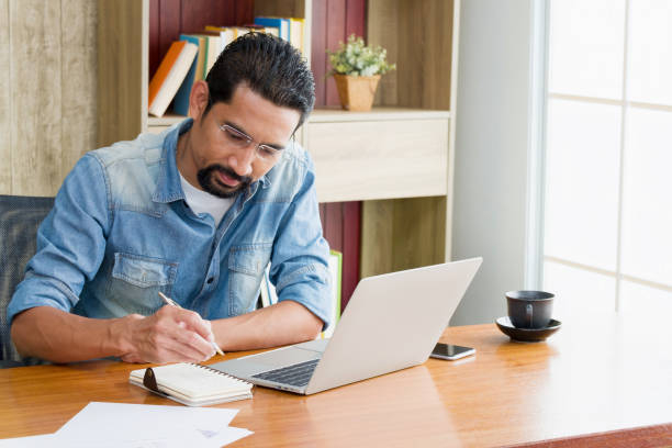istock Owner Business or Entrepreneur using a laptop for working and writing work schedules in the notebook while sitting at the desk in his home. 1225206148