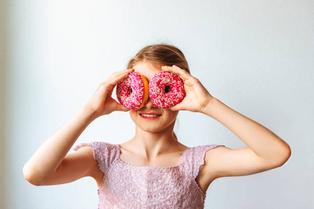 istock Little blond caucasian girl is having fun with donuts against white wall 1225209794