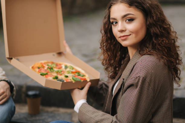 istock Woman open pizza box outdoors. Female hold open pizza box and smells appetizing 1225209951