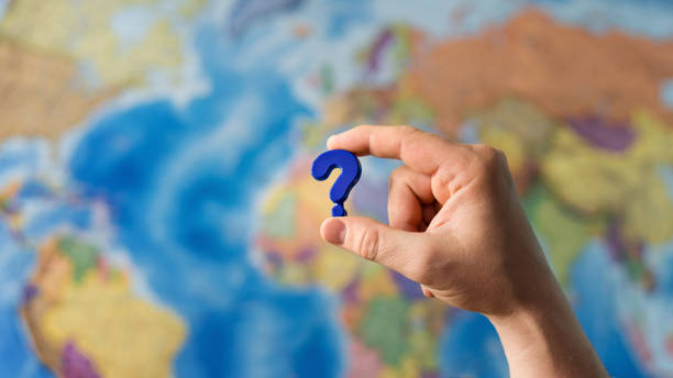Hand holding plastic toy Adult hand holding question mark plastic toy on the world political map background. Travel planning explore destination concept. Quarantine over, borders open mystery vacation stock pictures, royalty-free photos & images