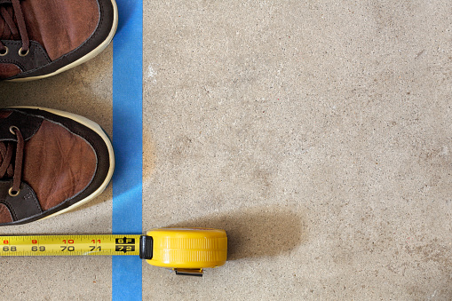 A high angle view of someone standing at a line marked with a piece of blue tape and a tape measure indicating the accepted six foot minimum for social distancing.