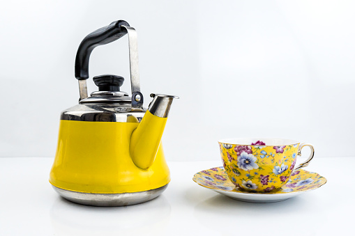 Yellow teapot and cup of tea on white glossy table
