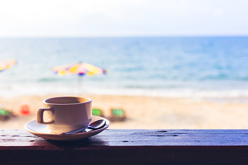 hot cup of coffee on the wood near the beach.