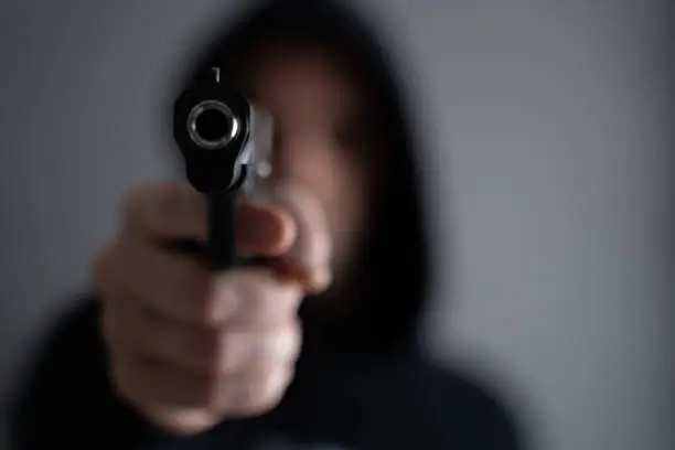 Criminal aiming gun camera, threatening burglar at victim.