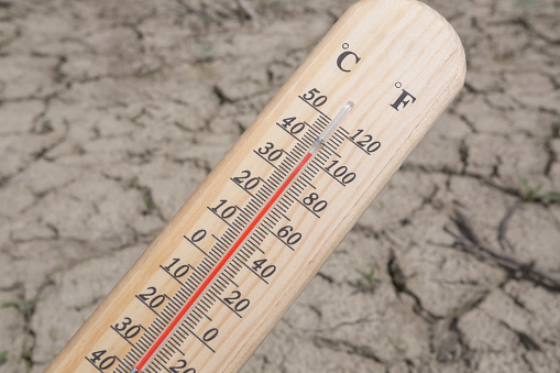 Thermometer with over one hundred degree Fahrenheit or almost 40 degree Celsius outdoor at barren cracked land on hot sunny summer day