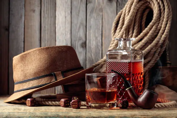 Strong alcoholic drink, pipe and dice on a old wooden table. In the background is a hemp rope and a man's hat. Concept for the big boys.