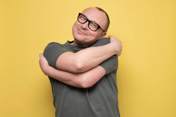 man smiling with pleasure embracing himself, keeping arms around his shoulders