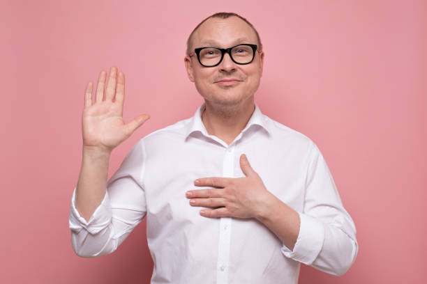 Mature man keeping hand on chest making promise, swearing to tell the truth Responsible mature man keeping hand on chest making promise, swearing to tell the truth, be honest dedicated. Studio shot on pink wall. pink promise stock pictures, royalty-free photos & images