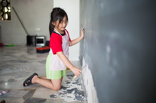 An Asia Chinese girl is helping family scraping the peel off part at the wall preparing for painting