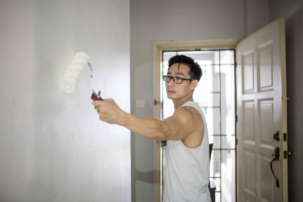 un uomo maturo cinese asiatico che dipinge pareti usando rullo di vernice nella sua nuova casa. concetto di restyling e ristrutturazione della casa. - paint roller copy space action adult foto e immagini stock