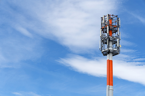 Red and white transmission mast against the blue sky with white clouds