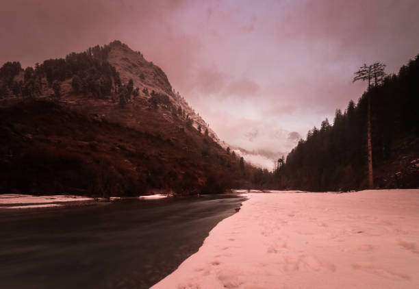Amazing view of sunset at the snow covered Parvati river, India along with the mountains in the distance. The camera faces east, 5K