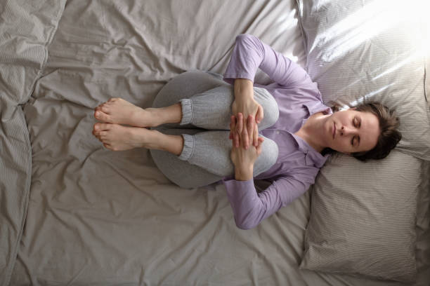 istock woman doing exercise for spine on bed, lying in Knees to Chest pose 1225255351