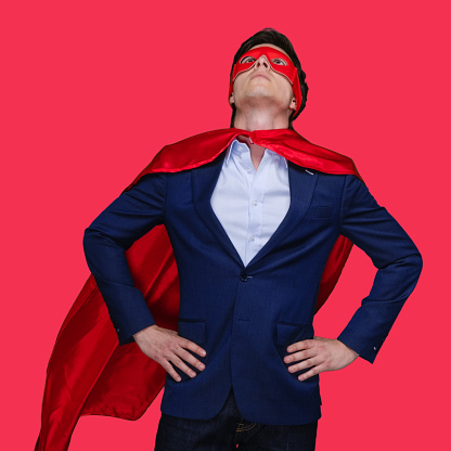 Waist up of aged 20-29 years old with short hair caucasian young male superhero standing in front of colored background wearing eye mask who is in concentration with hand on hip