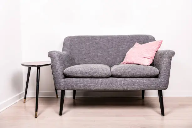 A cute gray settee with a pink pillow sitting on it, next to a small, contemporary occasional table.