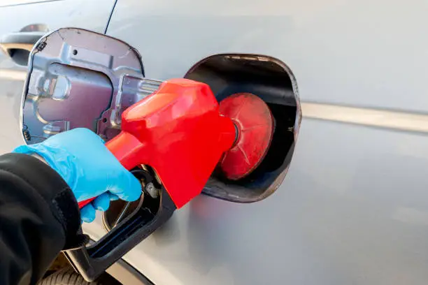 Hand wearing a blue personal protective glove pumps gas into an automobile. Shallow depth of field, focus on pump.