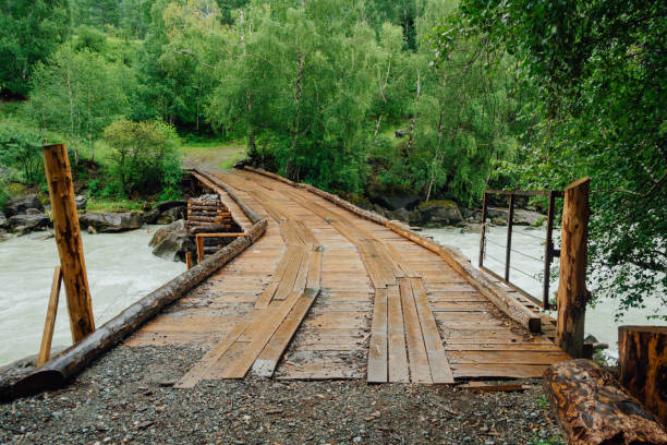 Wooden bridge of boards across mountain river. Rural old bridge in forest stock photo