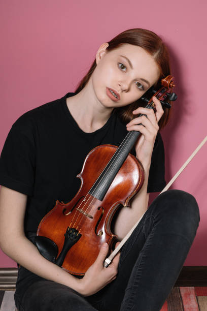 istock Girl in black plays violin on pink background 1225260933
