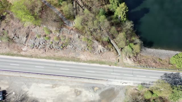 Aerial photograph of an arc-shaped flight over an asphalted country road with an embankment on which the raw rock of carbonaceous clay slate spreads out