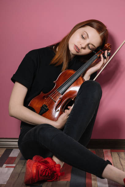 istock Girl in black plays violin on pink background 1225263300