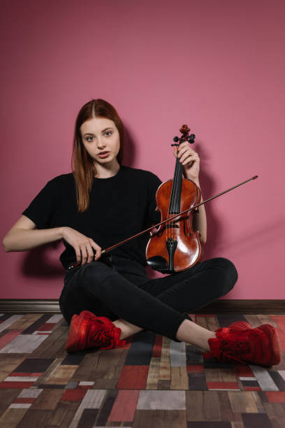 istock Girl in black plays violin on pink background 1225264961