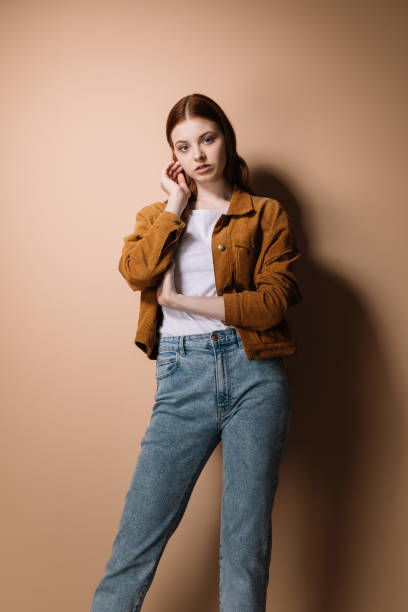 istock Girl in jeans and a brown jacket posing on a beige background 1225265649