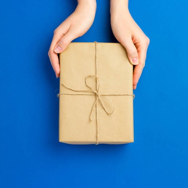 istock Top view of female hands holding present box package on Blue background. Zero waste shopping concept. Flat lay banner, top view, Sustainable lifestyle. Composition for birthday, mother day or xmas 1225265665