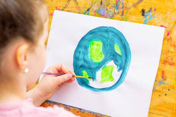 Child draws a planet Earth with a map of the world by watercolors on white paper on an easel. Peace and Earth day concept.