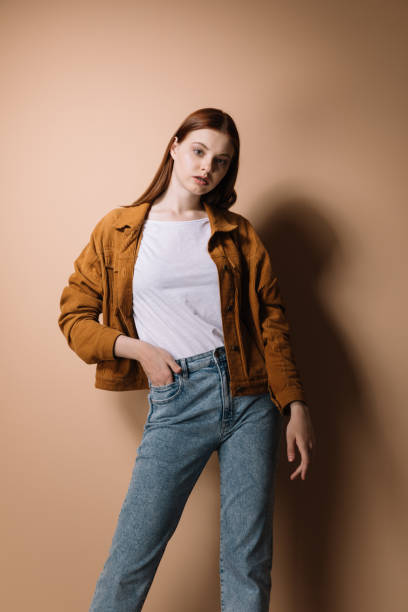 istock Girl in jeans and a brown jacket posing on a beige background 1225267582