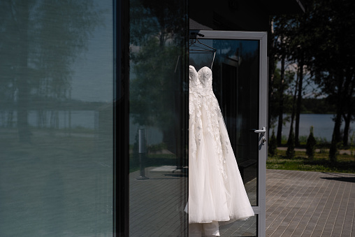 a white wedding dress is hanging on the glass door, good sunny weather, morning of the bride, morning before the wedding, bride's fees