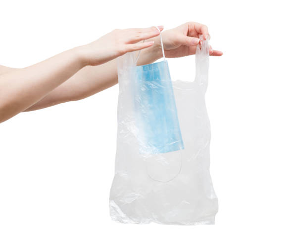 Woman is putting used disposal nonwoven safety mask in plastic bag before throwing it away. stock photo