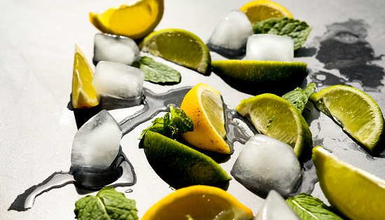 Fresh lime and lemon pieces, mint leaves and ice cubes on dark background. Summer drink or cocktail concept.