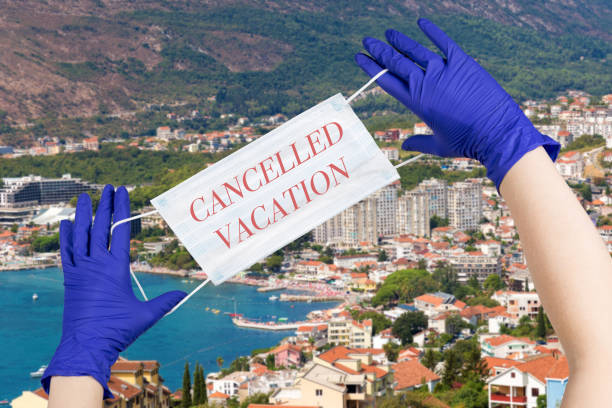 Woman hands with latex gloves on them are holding safety mask with sign cancelled vacation against Montenegro seaside background. stock photo
