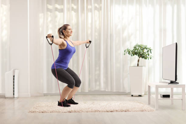 istock Young female exercising with a resistance band while watching tv 1225270732