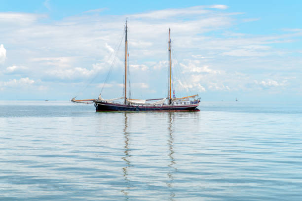 A two-masted ship is reflected on the surface of the water at sea