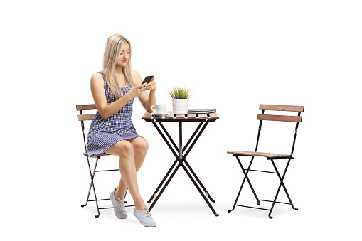 Young woman in a casual dress sitting at a cafe and using a mobile phone isolated on white background