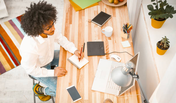 istock Copywriter working from Home. Creative young man writes notes in note pad looking at laptop. Arabic guy student in eyeglasses working or study. High angle view 1225274231
