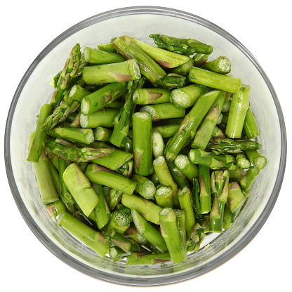 Diced Asparagus in clear Glass Bowl over white. Top view.