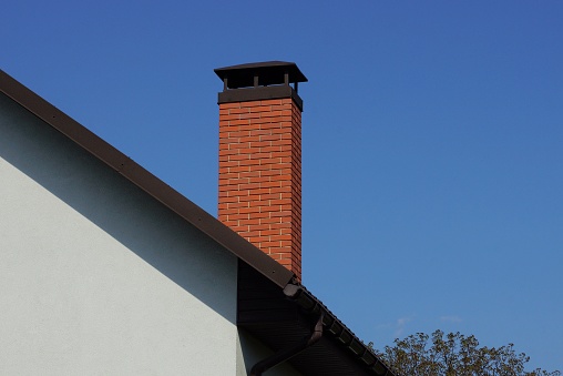 one long chimney of red bricks on the roof of the house against a blue sky