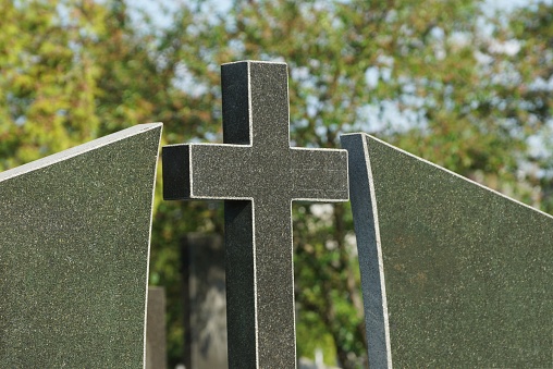 one black marble cross and part of the monument in the cemetery on a green background