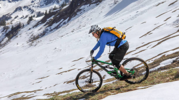 istock Mountain biker rides down snowy mountain ridge 1225280155