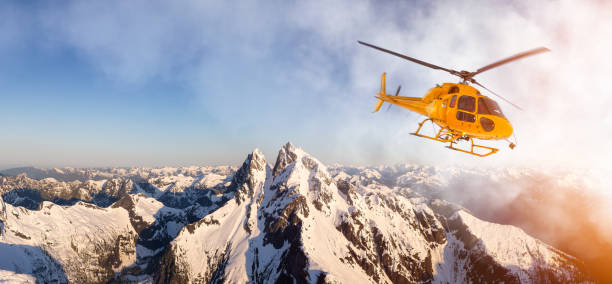 Yellow Helicopter flying over the Rocky Mountains during a sunny sunset. Aerial Landscape from British Columbia, Canada near Vancouver. Composite. Canadian Panoramic Nature Background
