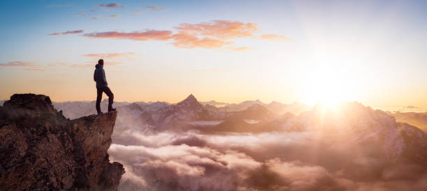 magical fantasy adventure composite of man hiking en la cima de una montaña rocosa - pico montaña fotografías e imágenes de stock