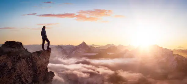 Magical Fantasy Adventure Composite of Man Hiking on top of a rocky mountain peak. Background Landscape from British Columbia, Canada. Sunset or Sunrise Colorful Sky