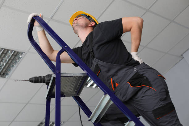 Repairman ladder with drill and looks at ceiling