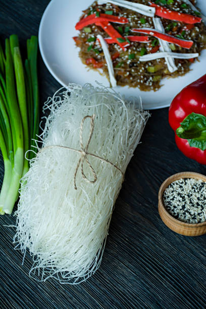 Asian cuisine. Fenchoza salad fried with vegetables, decorated with greens and crab sticks. Proper nutrition. Healthy food. View from above. Dark wooden background.