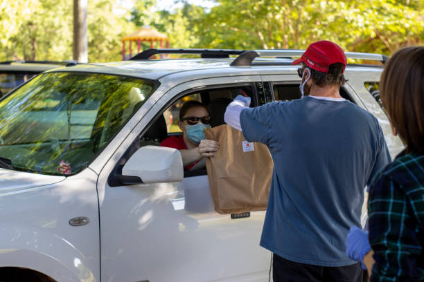 A volunteer wearing protective mask and gloves distributes a pre-paid order to a drive-up customer. stock photo