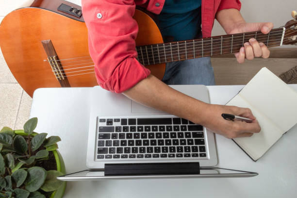 istock man takes notes from an online guitar class at home 1225300022