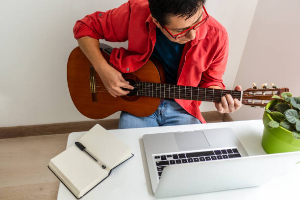 Man playing guitar in front of his computer at home